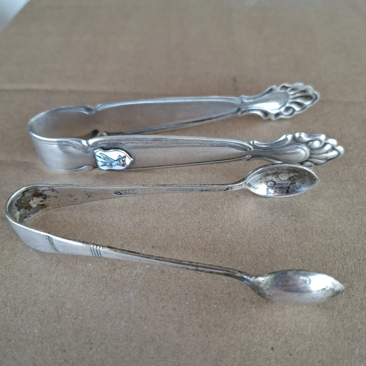 2 pairs Silver plate sugar tongs  1 with enamel crest